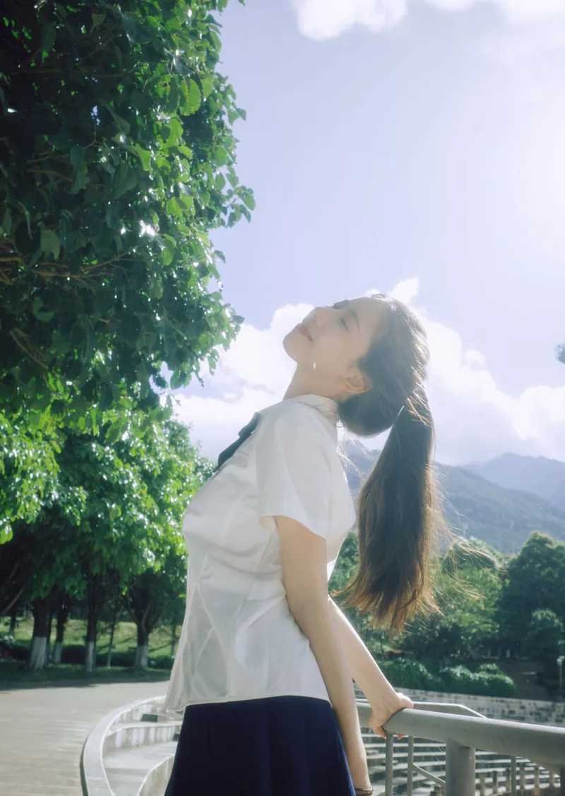 校园看台上仰着头的女孩，背后是山和云